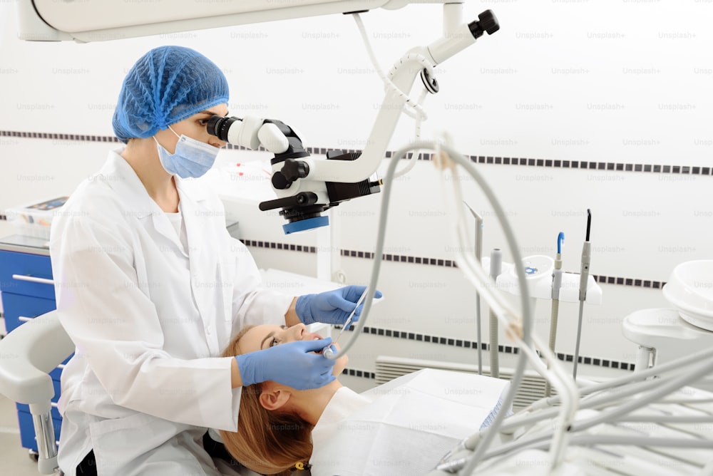 Female dentist looking at dental equipment and drilling in mouth of woman. Patient lying on chair and looking up
