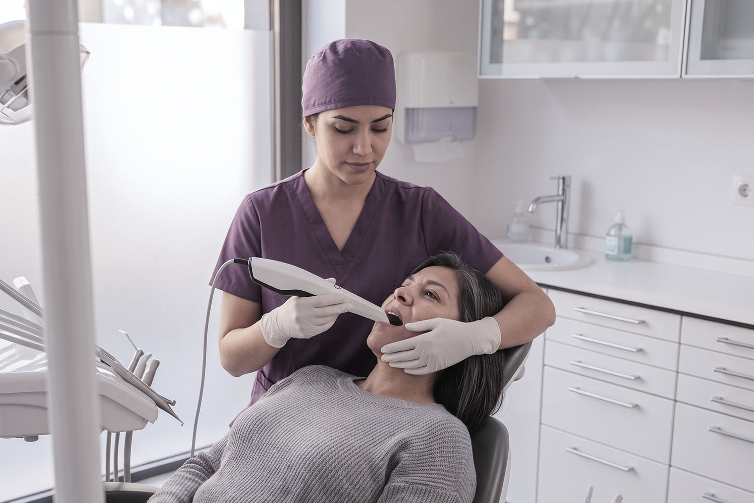 Dentista realizando un escaneo intraoral a una paciente en consultorio.